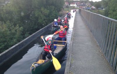 Group of people paddling in canoes along a narrow waterway with trees on the sides.